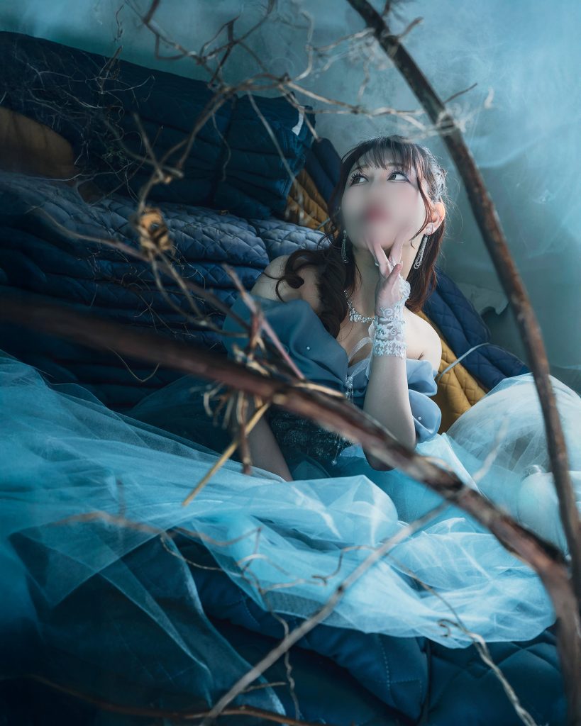 福岡の廃墟スタジオ『朝日陸運大川営業所』にて、フォトグラファー赤木友厚が撮影したポートレート。青いドレスを着たモデルAOIさんが、ガレキや枯れ枝の散乱する空間で、顎に手を当てて上を見上げている。青い光とスモークがちゃんみな『ハレンチ』MVの退廃的な世界観を再現している。顔にはぼかし処理。