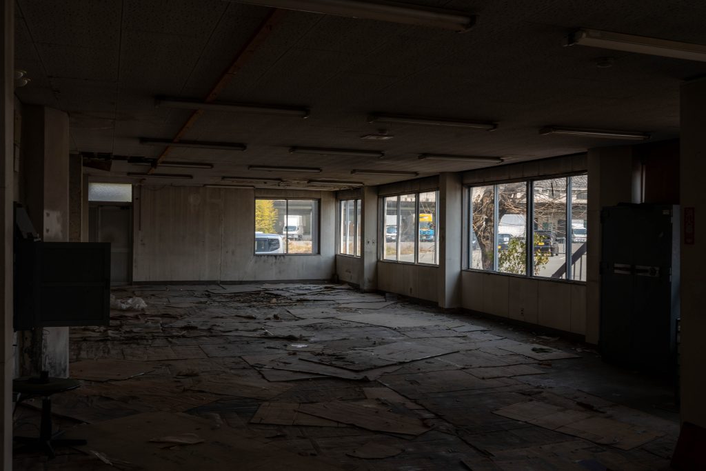 福岡県大川市の廃墟スタジオ『朝日陸運大川営業所』の広大な室内。床にはダンボールが散乱し、窓からは外のトラックが見える。暗がりに差し込む光がドラマチックな、ちゃんみな『ハレンチ』MV再現ポートレートのロケーション風景。