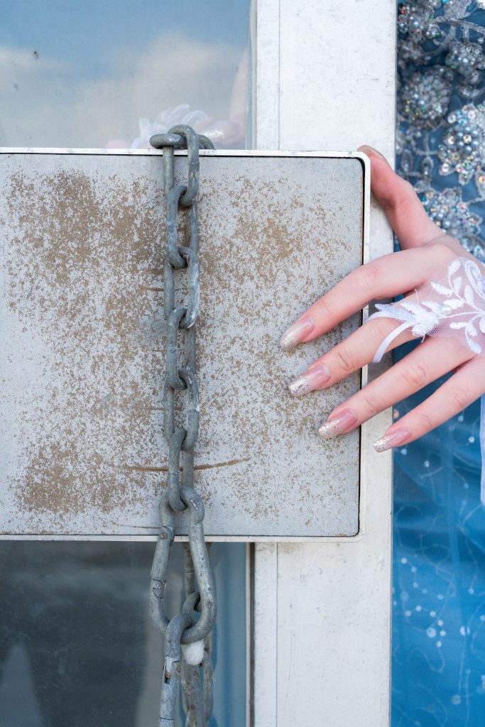 錆びた鉄板と鎖の前に、白いレースのグローブをはめたモデルAOIさんの手が添えられている。背景には青いドレスが見える。無機質な廃墟の質感と女性らしい繊細なディテールの対比。ちゃんみな『ハレンチ』の世界観を表現したイメージカット。