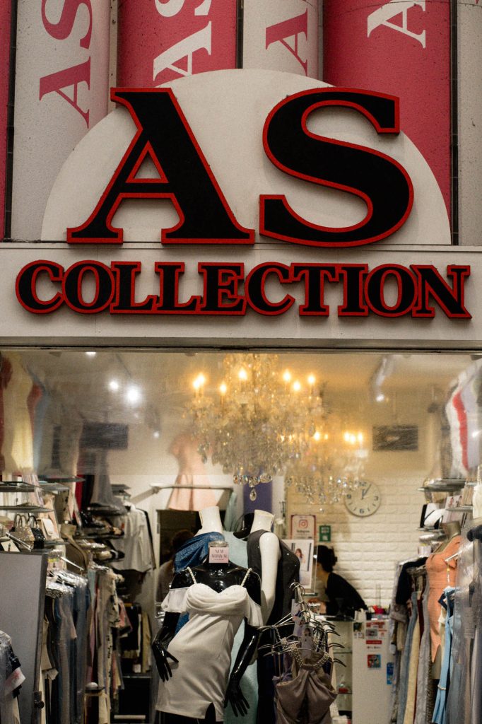 上川端商店街にあるナイトワーク向けドレスショップ「AS COLLECTION」の店頭。店内の豪華なシャンデリアと、白いドレスを着たマネキンがライトアップされている。