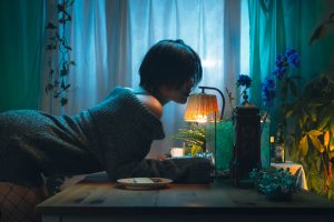 夜の静寂を思わせるブルーのライティング。ランプの灯りの傍で佇む女性。人生の成熟と内省、穏やかな終末を表現したローキーなポートレート。九州PMD2024でSilverを受賞した赤木友厚の作品。