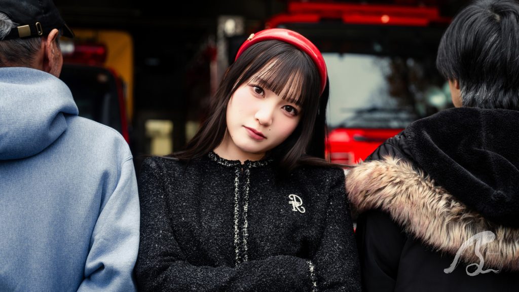 博多消防署冷泉出張所の消防車と建物を背景に、モデルのぴよさんが中央に立つポートレート写真。彼女は黒いツイードジャケットと赤いカチューシャを着用し、腕を組んでカメラを見つめている。彼女の左右には、背中を向けた2人の人物が並んでおり、画面に奥行きを加えている。背景には赤い消防車が見え、消防署のシャッターや窓も写っている。右下には「JS」の透かしが入っている。