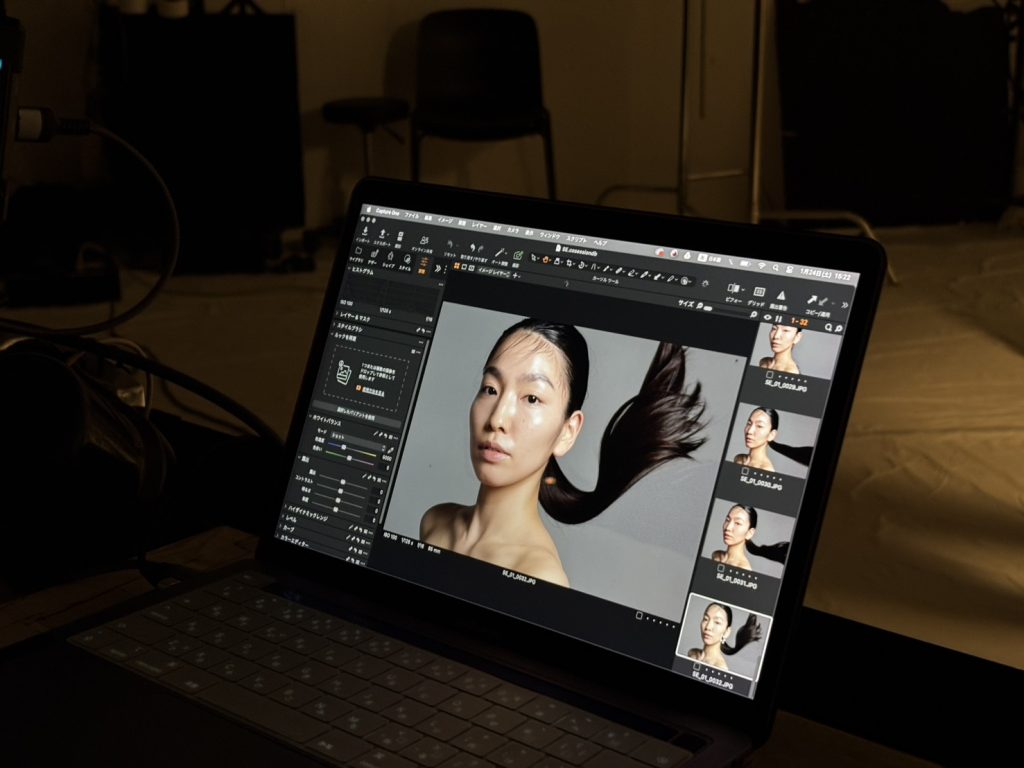 薄暗いスタジオで、ノートPC（MacBook Pro）の画面にCapture Oneのインターフェースが表示され、モデル（女性）のポートレートがプレビューされている。]