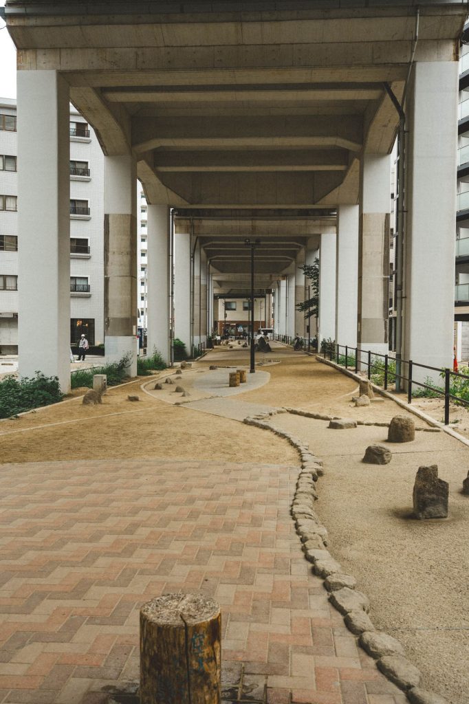 高架下にある、コンクリートの巨大な柱が並ぶ砂利敷きの遊歩道。