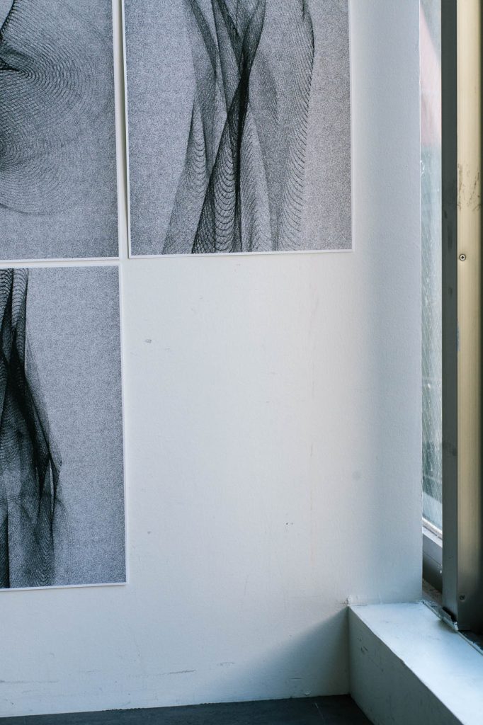 壁面に整然と並べられたモノクロの抽象写真作品。細かな粒子と流動的な線が特徴。