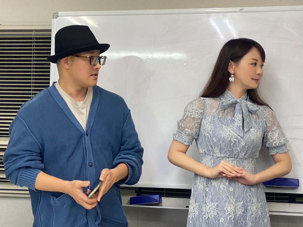 ホワイトボードの前で談笑する、黒い帽子の赤木友厚とモデルの宮崎舞子さん