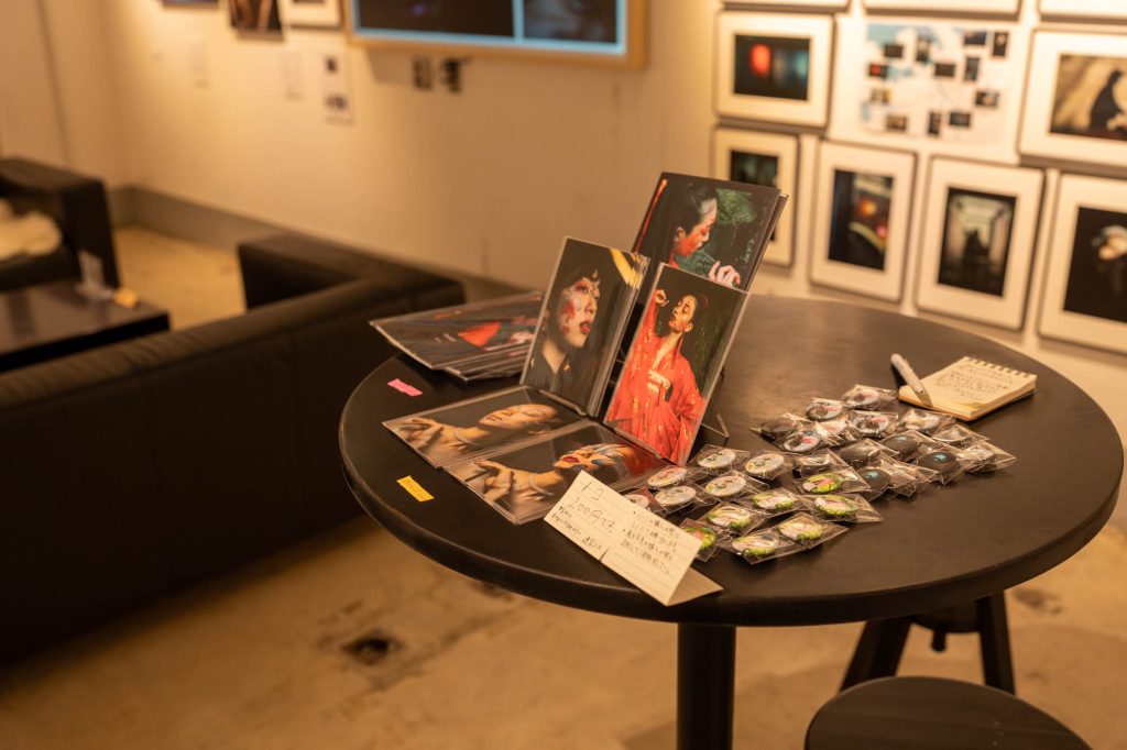 カフェテーブルの上にディスプレイされた、写真展出展作家のオリジナルポストカードや缶バッジなどの物販グッズ