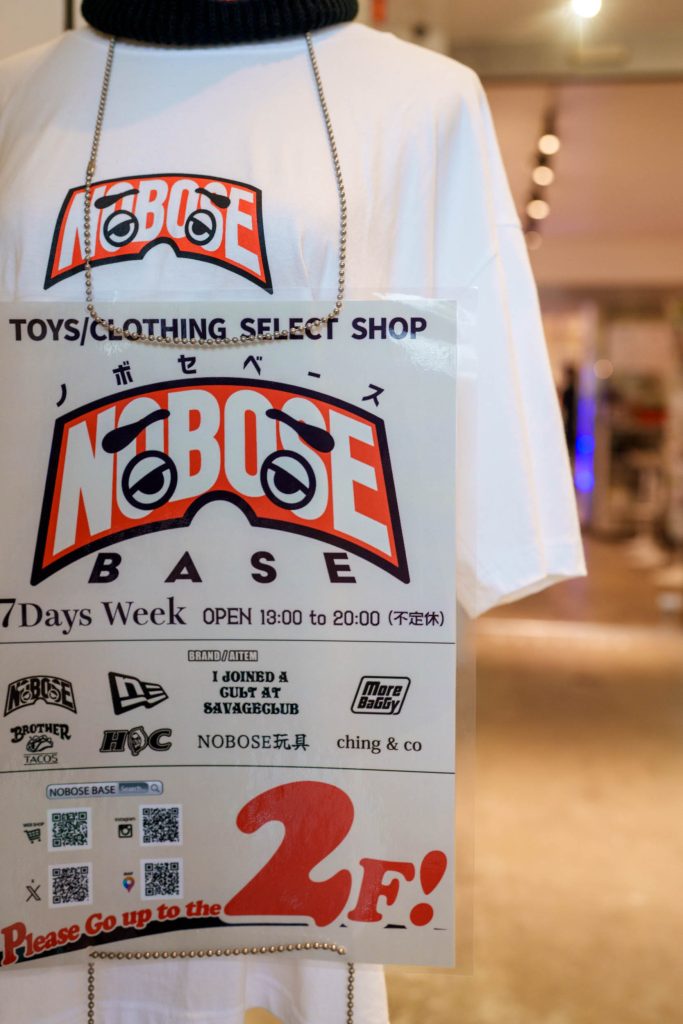 ART BASE KMYの店内に飾られた「NOBOSE BASE」のロゴ入りTシャツと、2階のセレクトショップを案内するポップなポスター