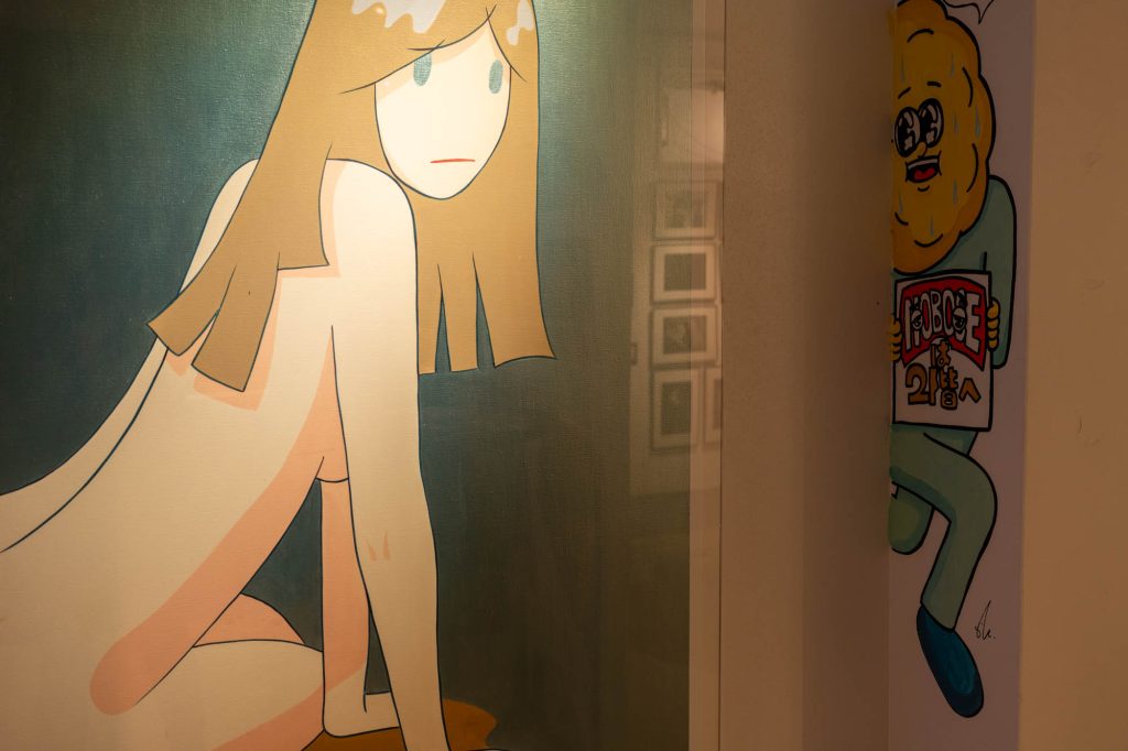 壁面に展示された女性のイラストアートと、その奥の壁から覗くように描かれた「NOBOSEは2階へ」という文字を持つキャラクターのイラスト